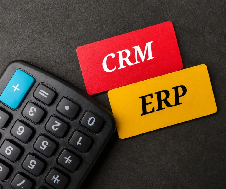 Plytelės su užrašais „CRM“ ir „ERP“ ant stalo su skaičiuotuvu