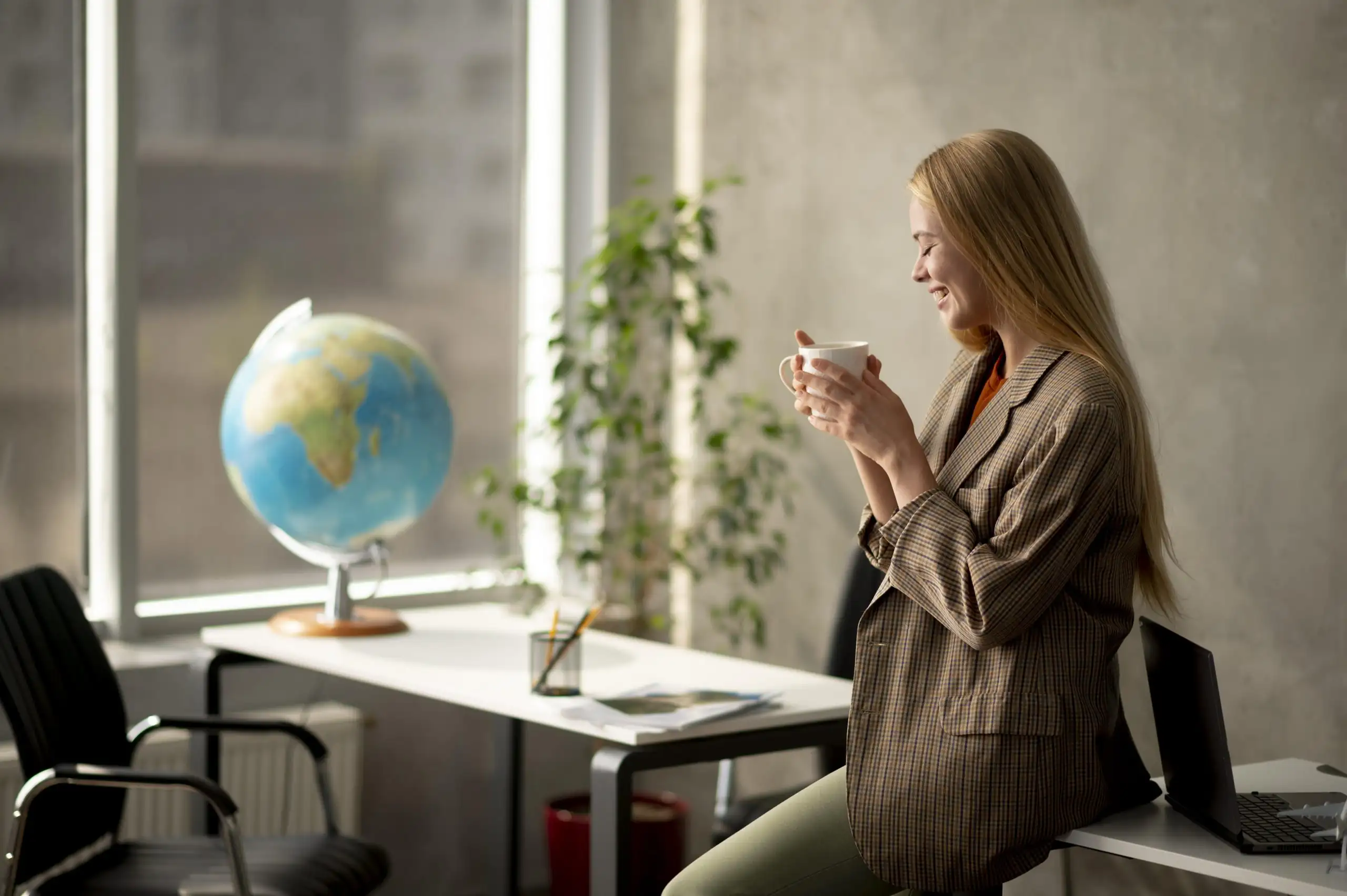 A woman sitting in a classroom near a globe drinking coffee